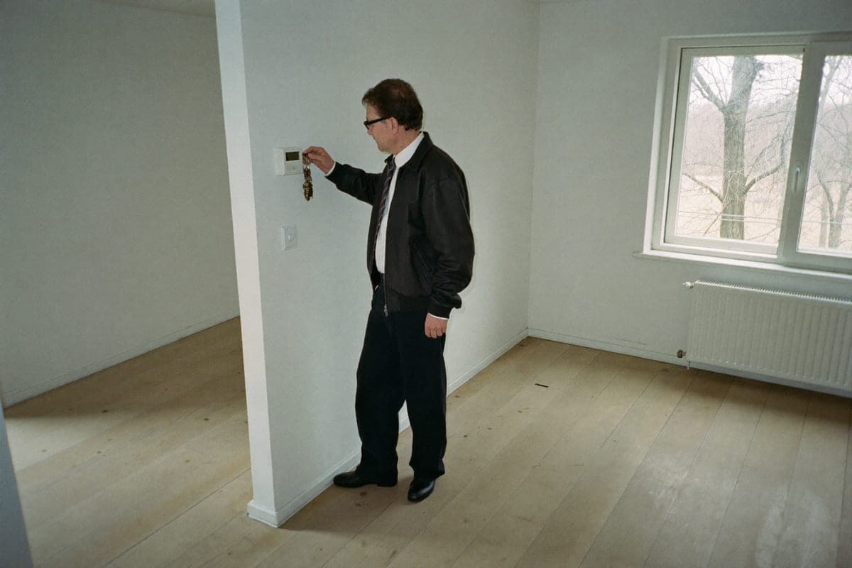 A landlord standing in an empty, freshly painted flat between tenancies, checking the wall thermostat with the keys in his hand.